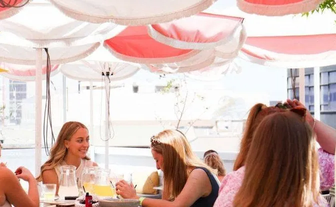 Friends sharing jugs of cocktails under pink and white umbrellas on the Humber rooftop