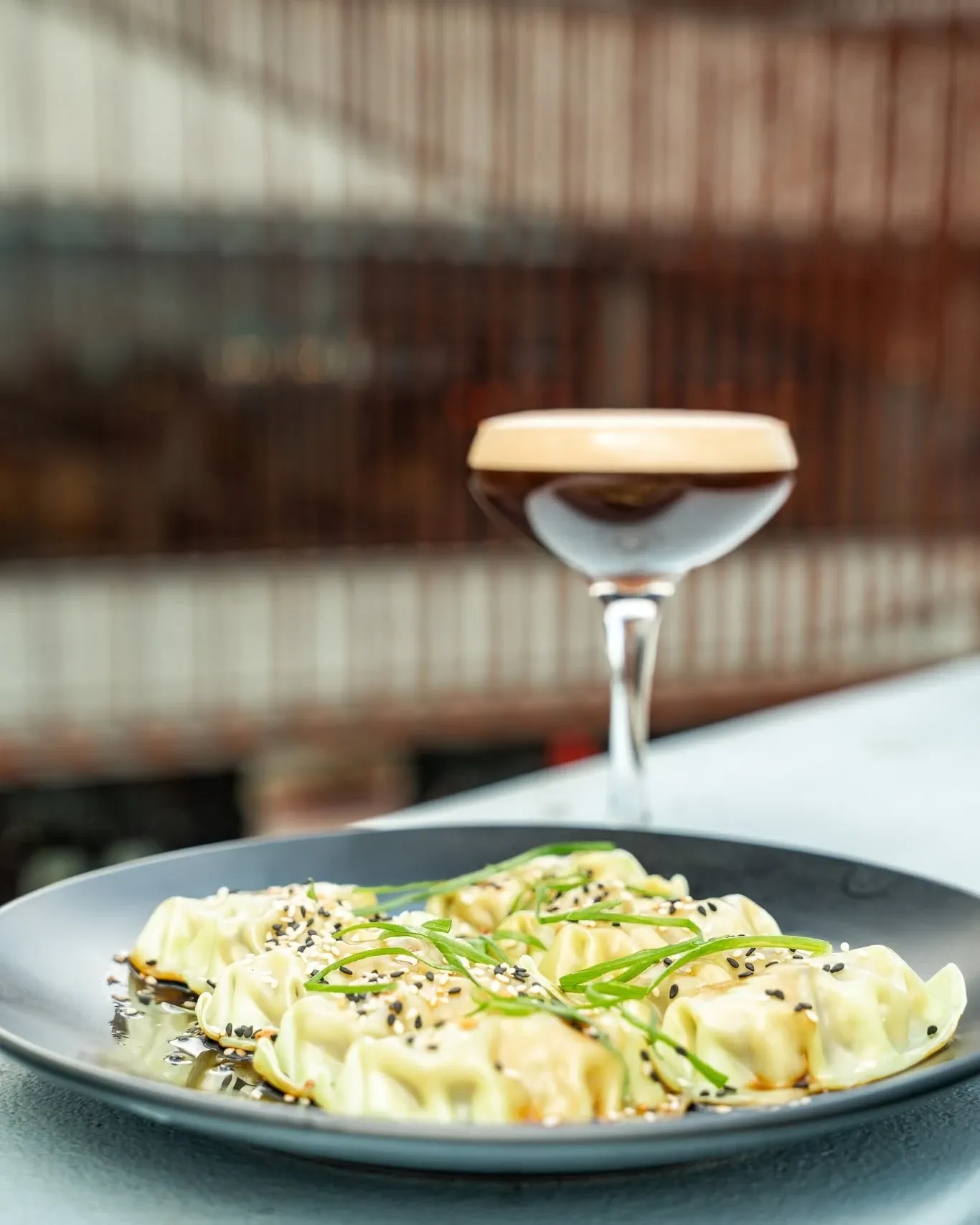 A plate of dumplings with sesame seeds and spring onion, with an espresso martini behind it on the Humber rooftop bar